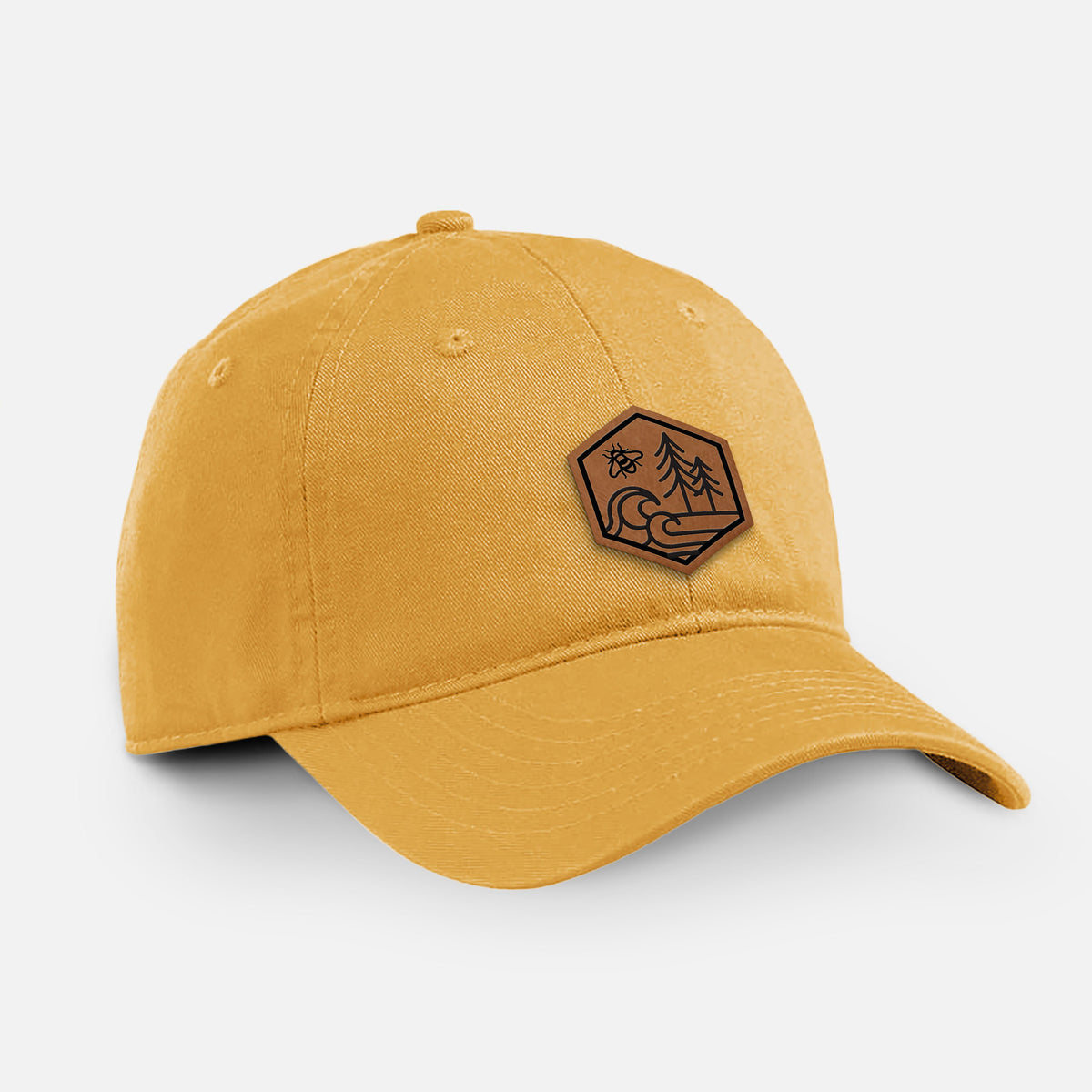 Beehive yellow cotton baseball hat with a brown leather hexagon patch engraved with a bee, ocean waves and pine trees on the front.