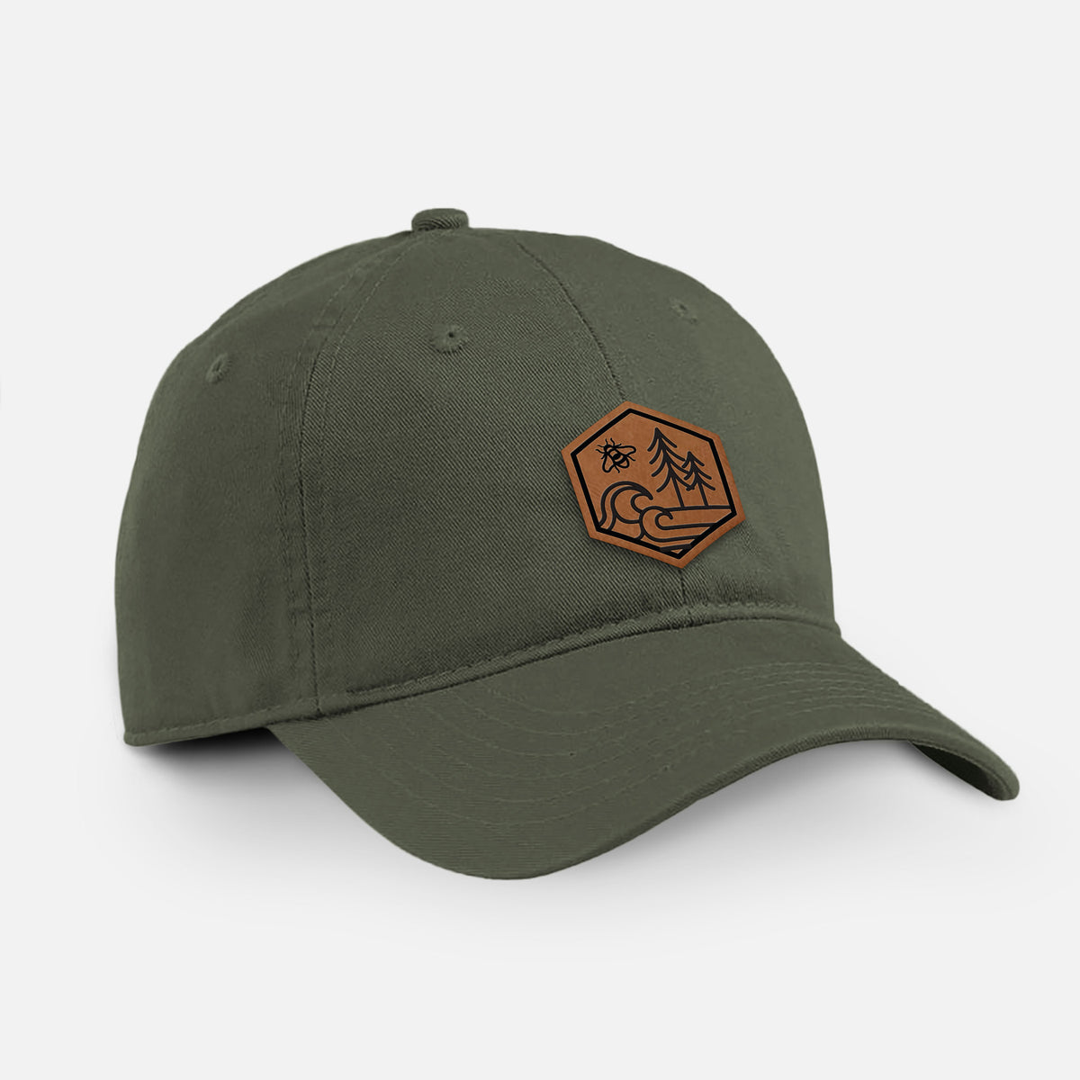 Olive cotton baseball hat with a brown leather hexagon patch engraved with a bee, ocean waves and pine trees on the front.