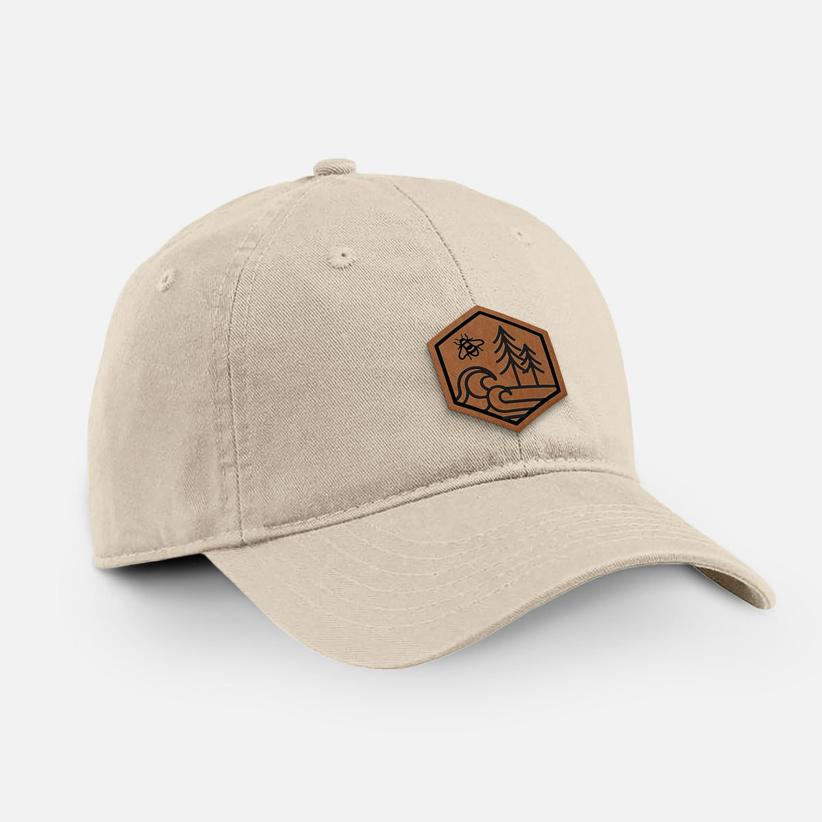 Stone cotton baseball hat with a brown leather hexagon patch engraved with a bee, ocean waves and pine trees on the front.