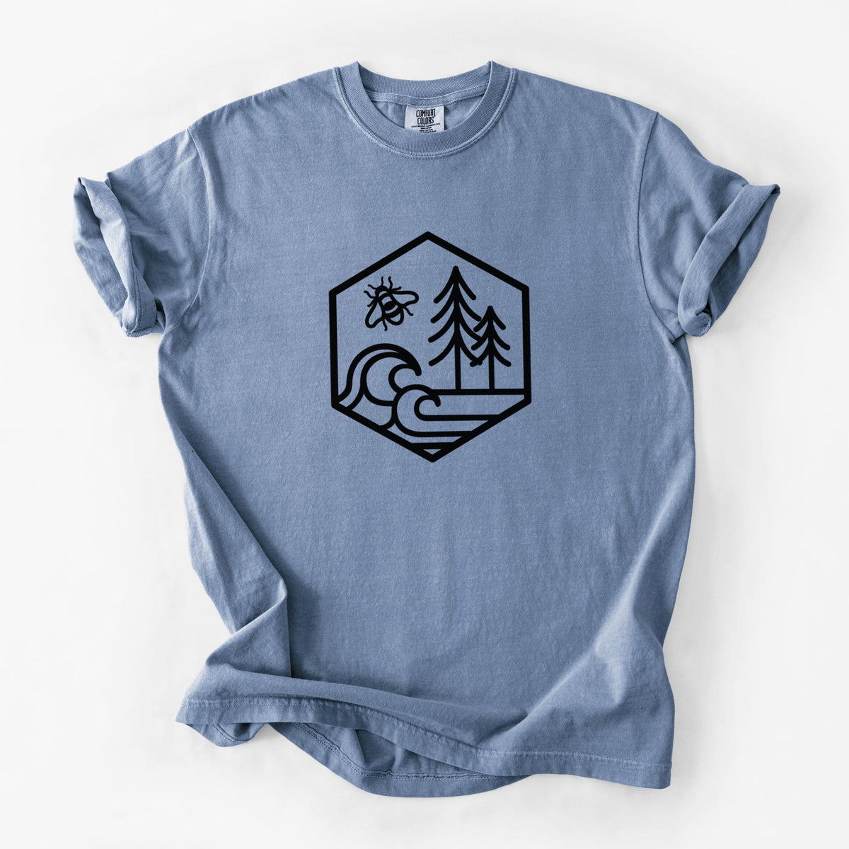 Blue jean Comfort Colors t-shirt laid flat, printed with a black line art hexagon holding a bee, ocean waves and pine trees.
