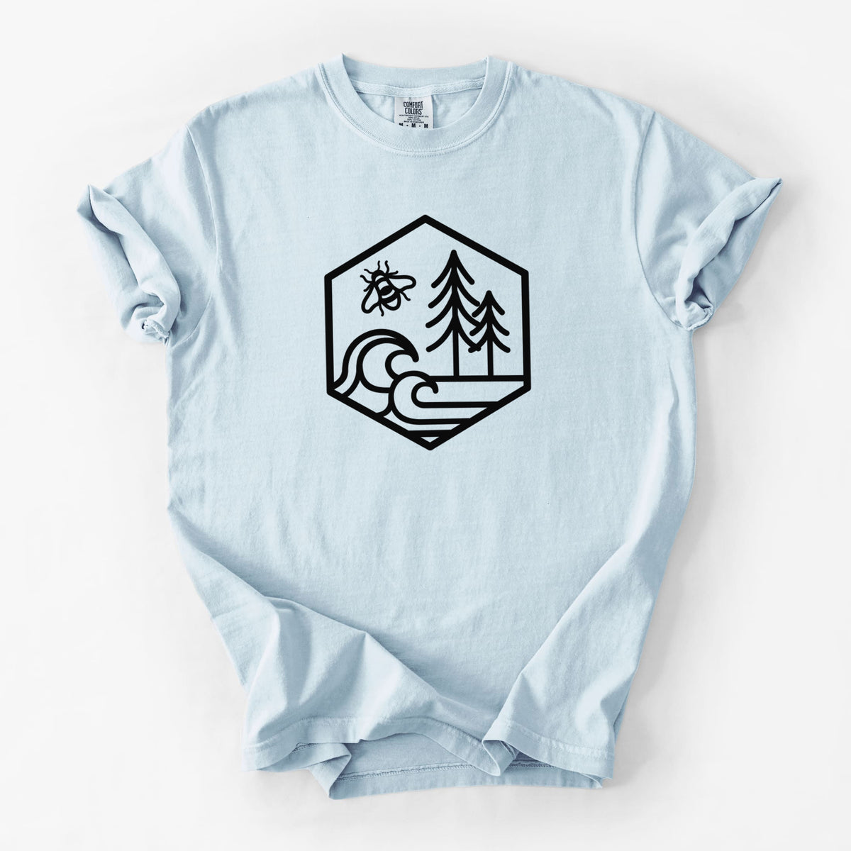 Chambray blue Comfort Colors t-shirt laid flat, printed with a black line art hexagon holding a bee, ocean waves and pine trees.