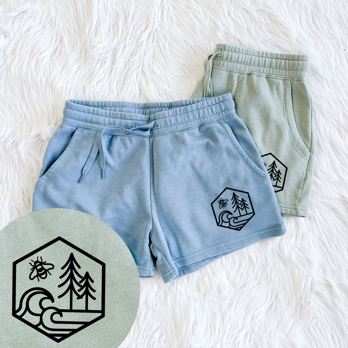 Two pairs of Cali Wave shorts in different colors printed with a black line art hexagon holding a bee, ocean waves and pine trees, with a close-up of the print.