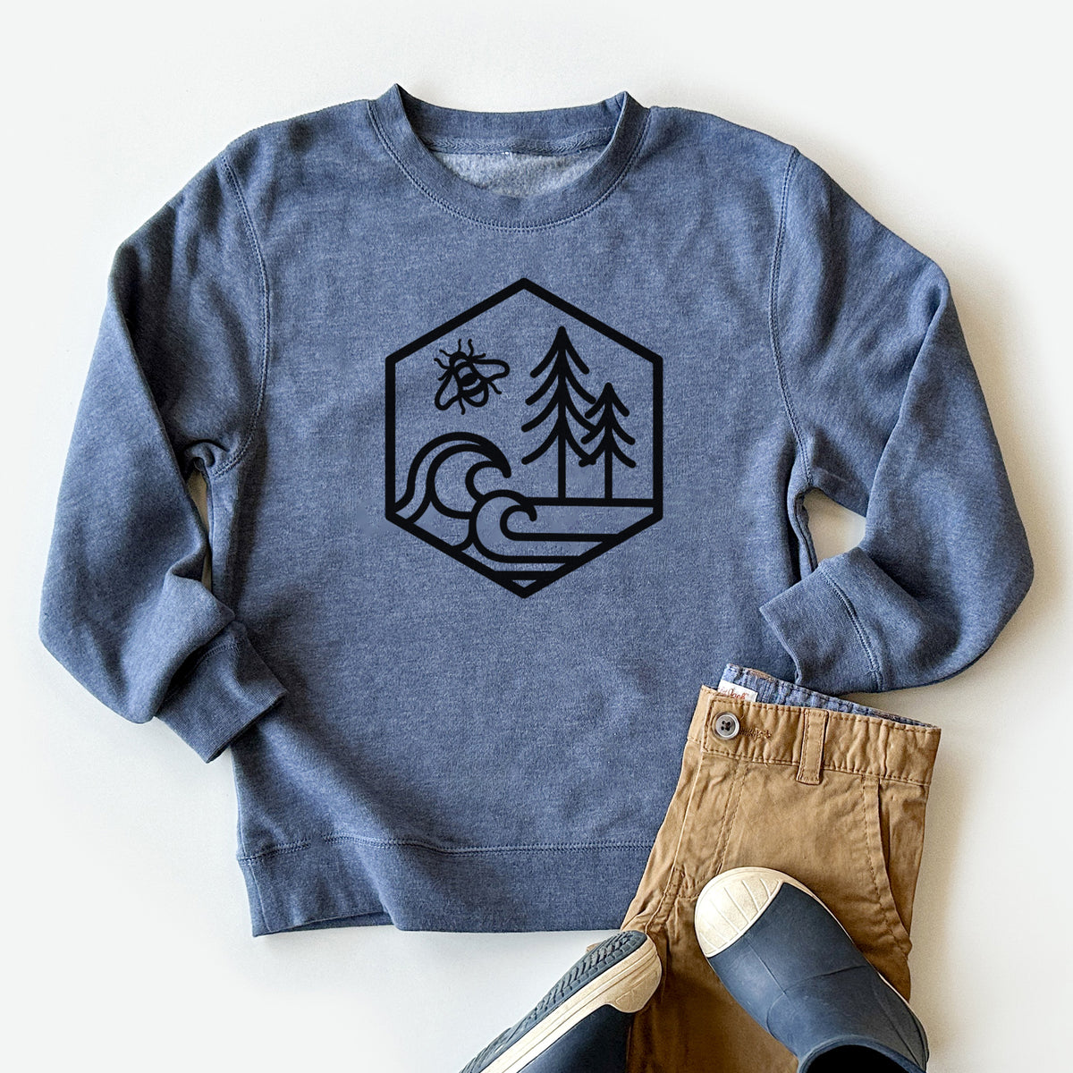 Youth crewneck sweatshirt printed with a black line art hexagon holding a bee, ocean waves and pine trees, styled flat with khaki pants and shoes.