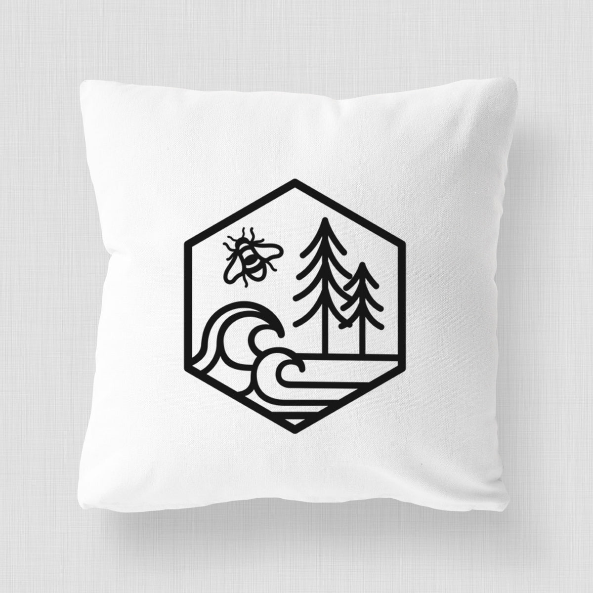 White pillow cover printed with a black line art hexagon holding a bee, ocean waves and pine trees.