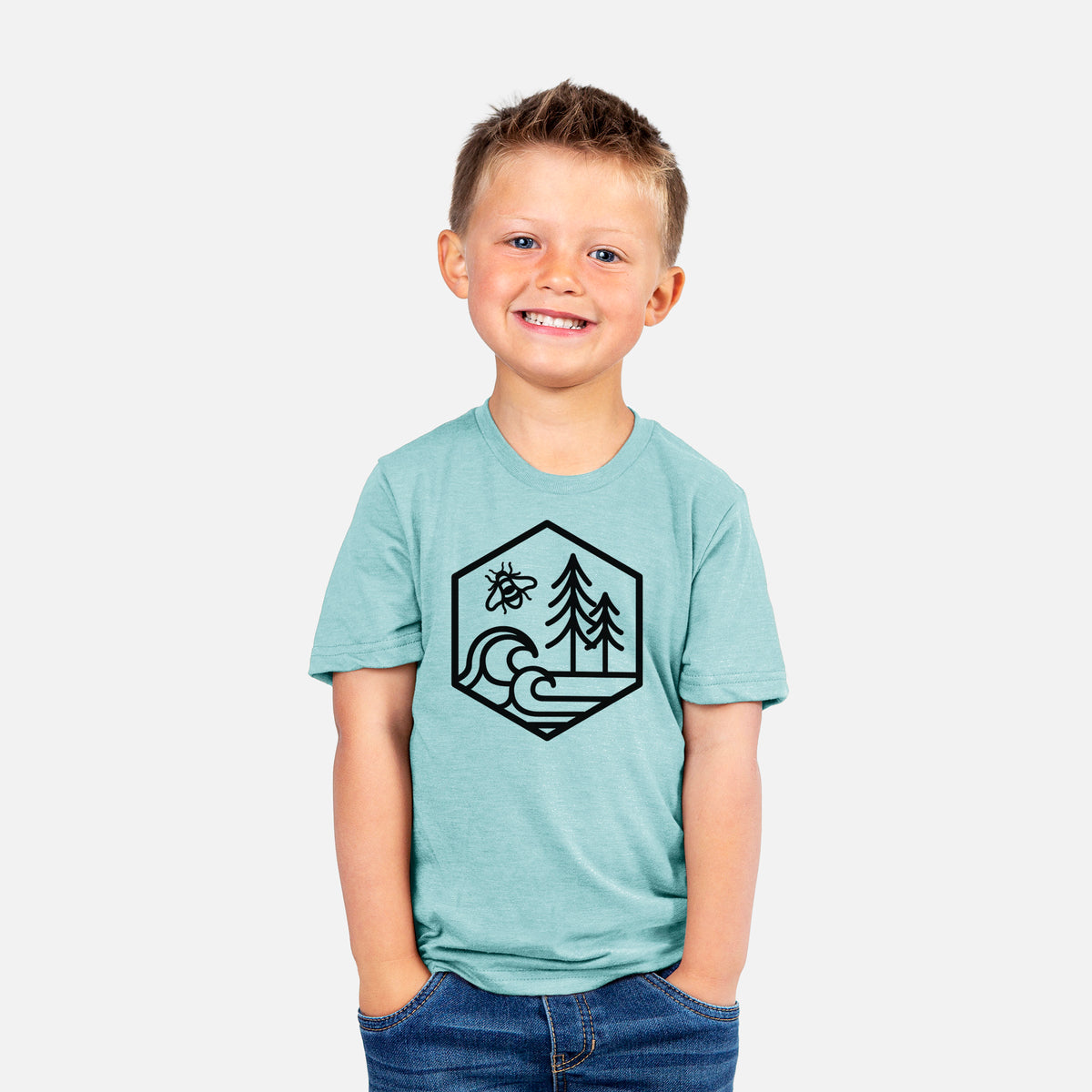 Smiling boy wearing a youth t-shirt printed with a black line art hexagon holding a bee, ocean waves and pine trees.