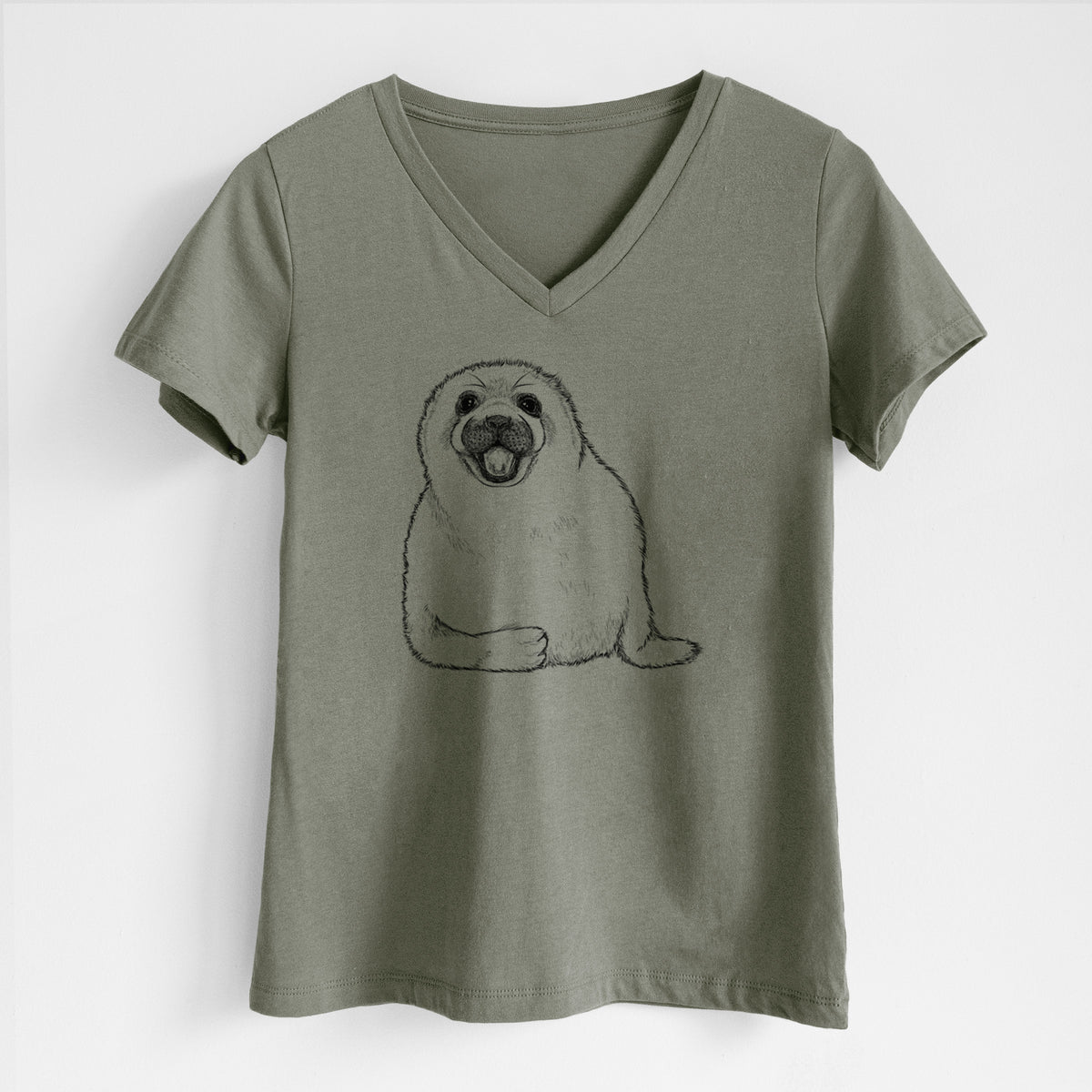 Military green women's relaxed fit cotton V-neck t-shirt laid flat, printed with a black ink illustration of a smiling harp seal pup lying down.