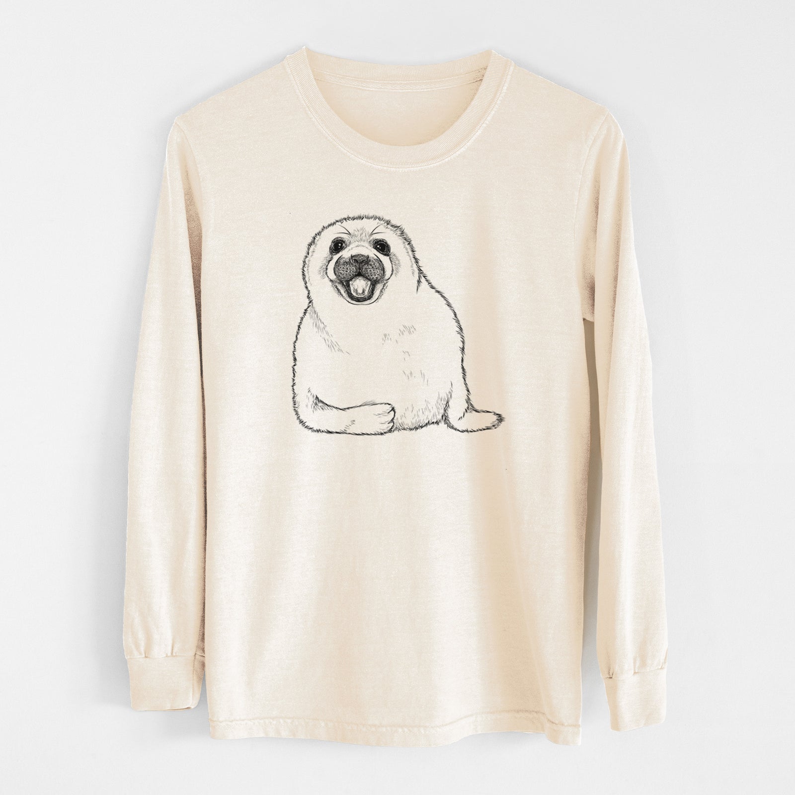 Ivory Comfort Colors long sleeve shirt laid flat, printed with a black ink illustration of a smiling harp seal pup lying down.