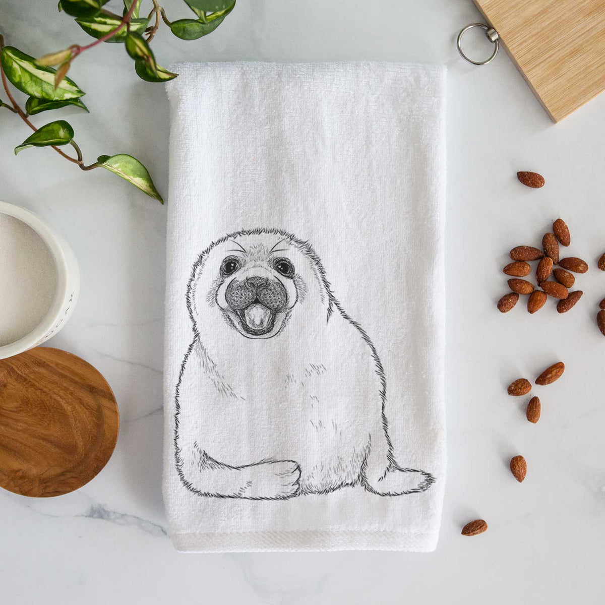 White hand towel printed with a black ink illustration of a smiling harp seal pup lying down.