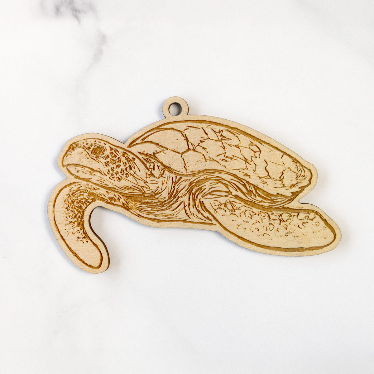 Wooden ornament featuring a engraving of a hawksbill sea turtle swimming, with a patterned shell, on a marble surface.