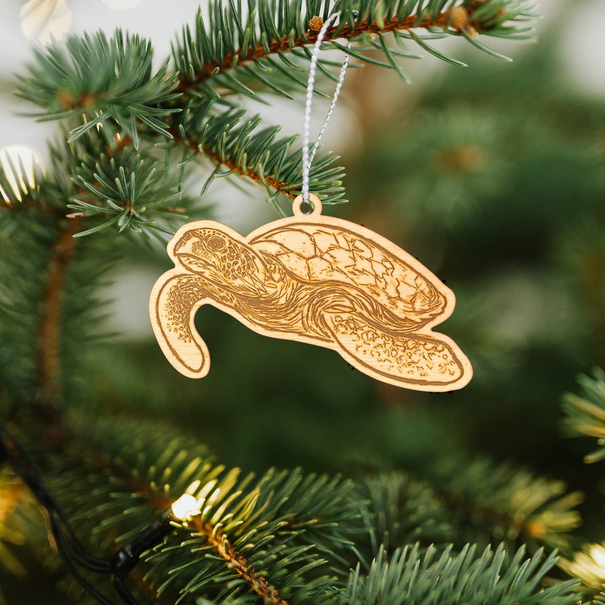 Wooden ornament featuring a engraving of a hawksbill sea turtle swimming, with a patterned shell, hanging on a Christmas tree.