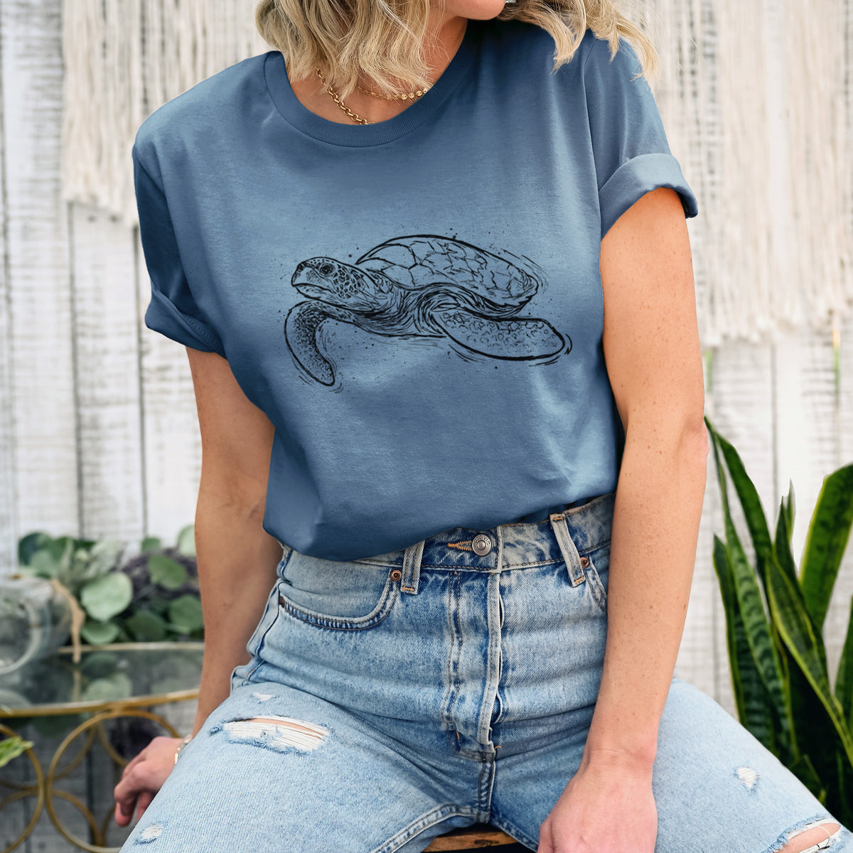 Woman wearing a steel blue lightweight cotton t-shirt printed with a black ink illustration of a hawksbill sea turtle swimming, with a patterned shell.
