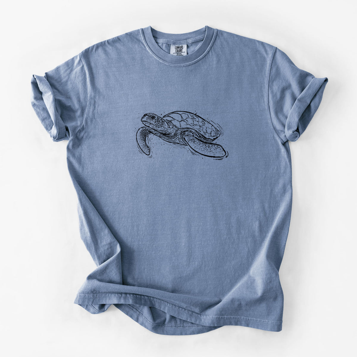 Blue jean Comfort Colors t-shirt laid flat, printed with a black ink illustration of a hawksbill sea turtle swimming, with a patterned shell.