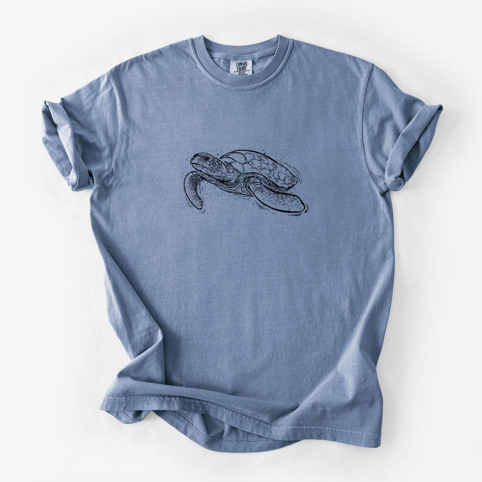 Blue jean Comfort Colors t-shirt laid flat, printed with a black ink illustration of a hawksbill sea turtle swimming, with a patterned shell.
