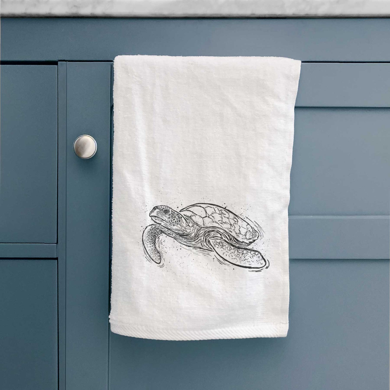 White hand towel printed with a black ink illustration of a hawksbill sea turtle swimming, with a patterned shell.