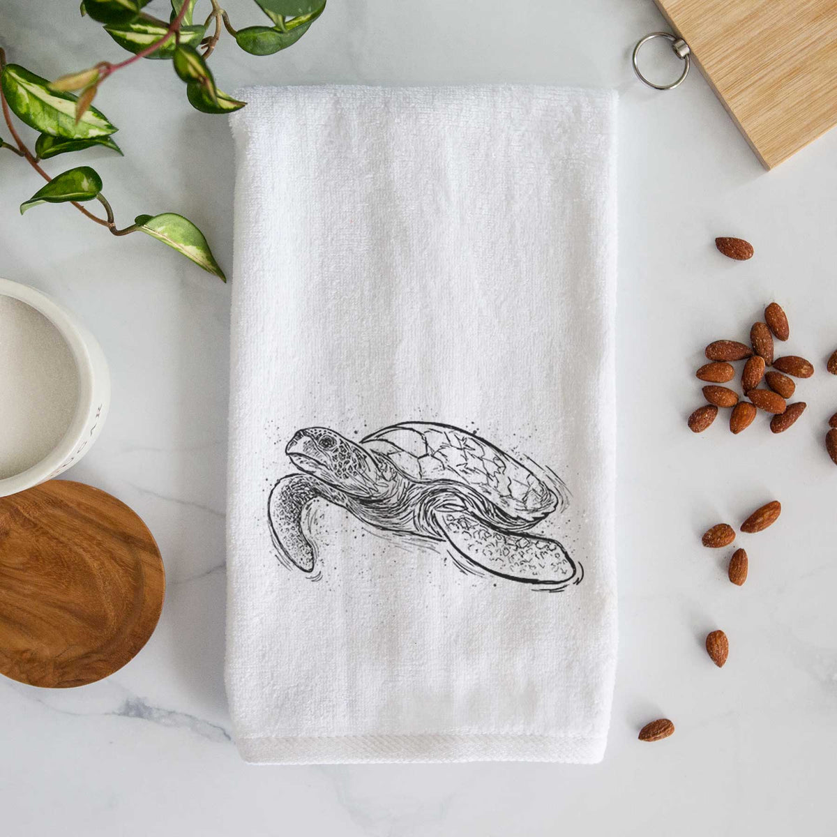 White hand towel printed with a black ink illustration of a hawksbill sea turtle swimming, with a patterned shell.