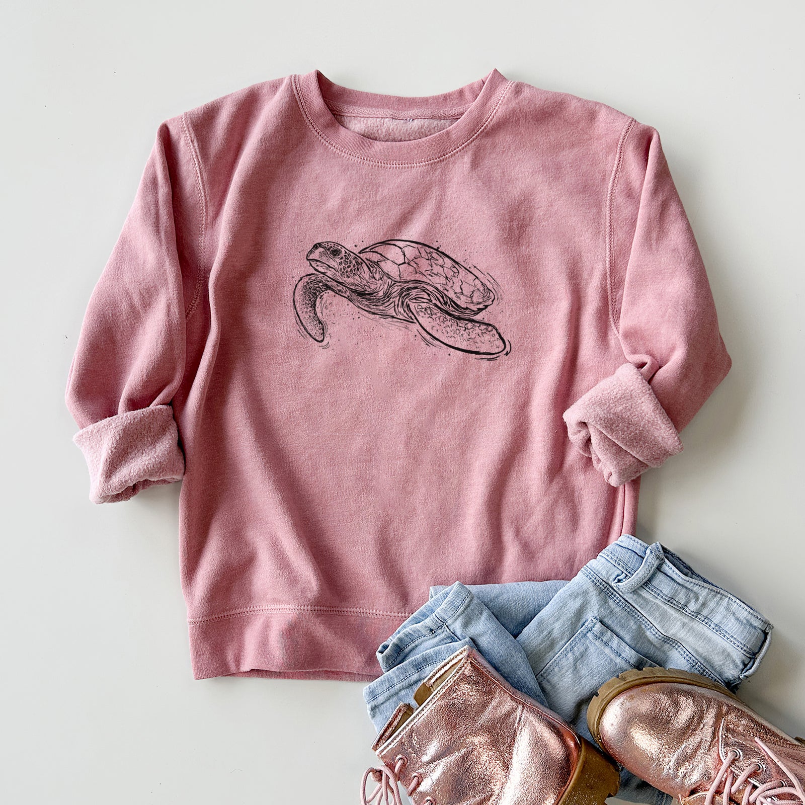 Boy wearing a youth crewneck sweatshirt printed with a black ink illustration of a hawksbill sea turtle swimming, with a patterned shell, outdoors.