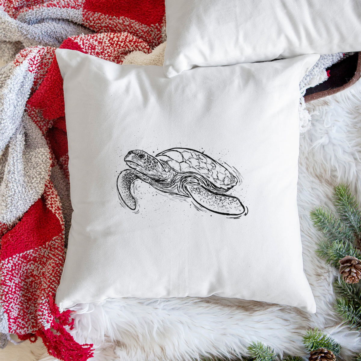 White pillow cover printed with a black ink illustration of a hawksbill sea turtle swimming, with a patterned shell, on a woven chair.