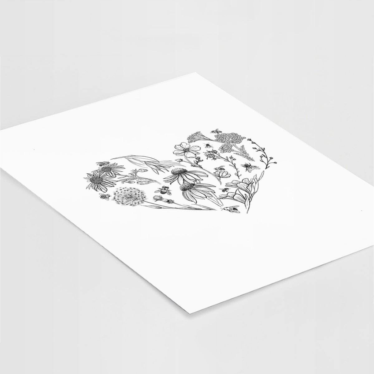 Art print of a heart shape filled with black ink flowers and bees, lying at an angle on a white surface.