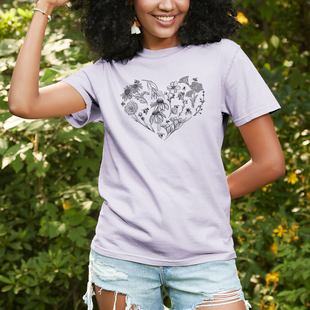 Woman wearing a Comfort Colors t-shirt printed with a heart shape filled with black ink flowers and bees, outdoors.