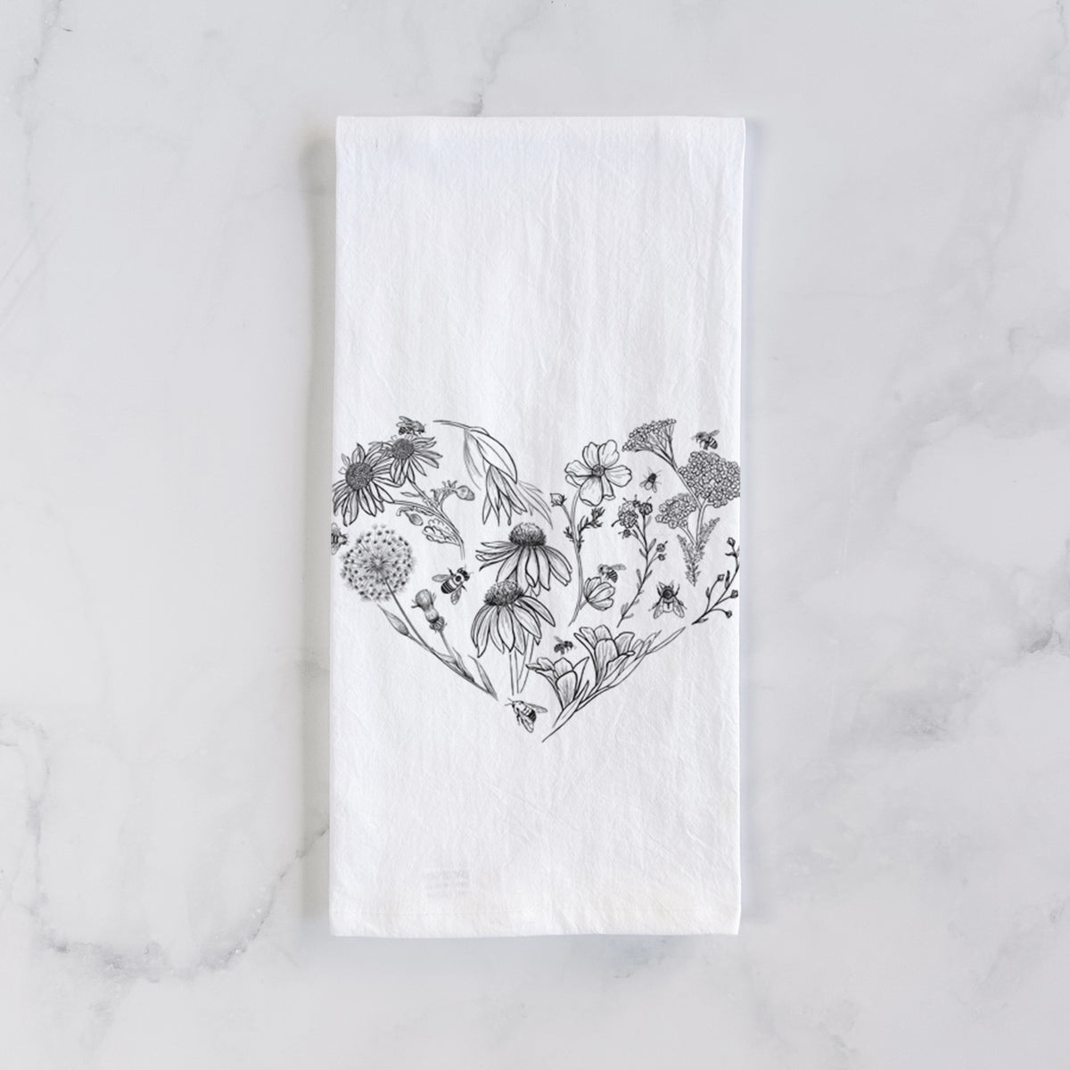 White cotton tea towel laid flat on marble, printed with a heart shape filled with black ink flowers and bees.