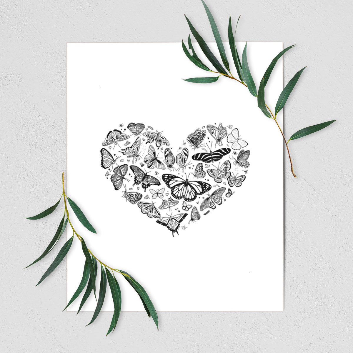 Art print of a heart shape filled with small black ink butterflies and moths, shown with eucalyptus leaves.