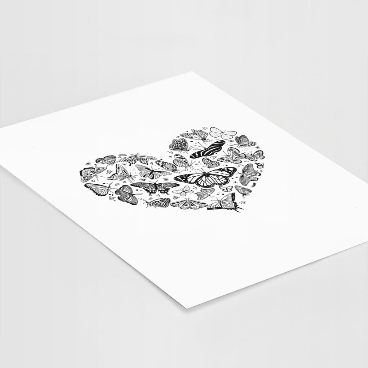 Art print of a heart shape filled with small black ink butterflies and moths, lying at an angle on a white surface.