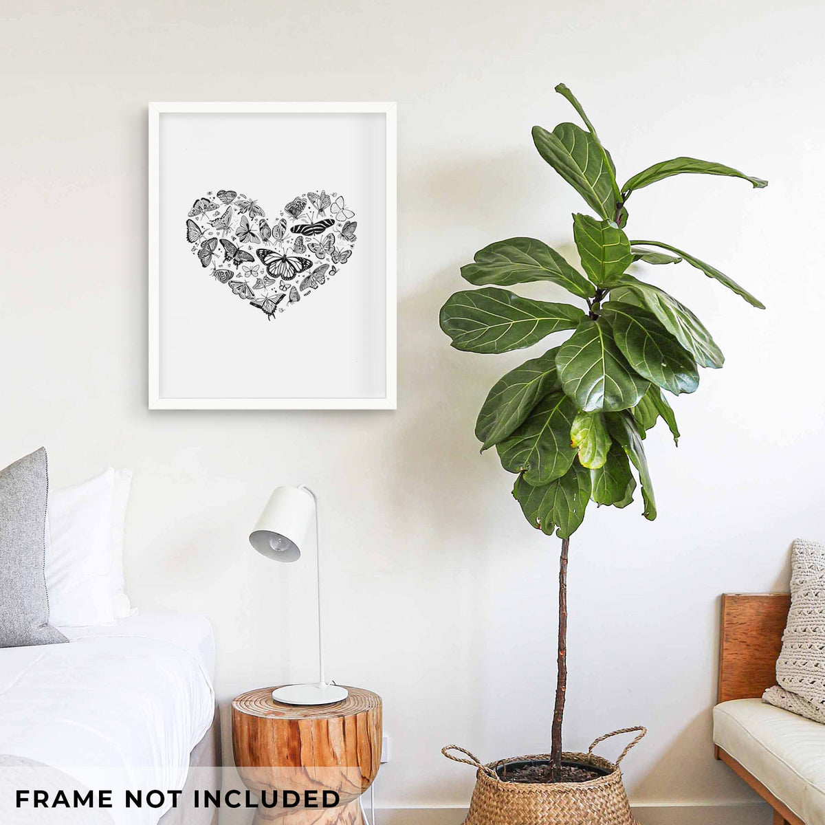 Art print of a heart shape filled with small black ink butterflies and moths, shown framed on a living room wall beside a potted plant. Frame not included.