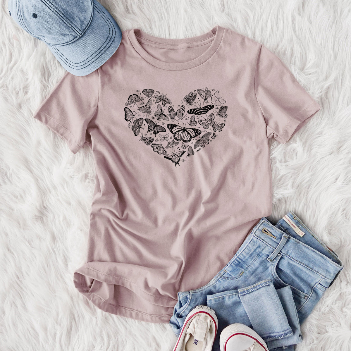 Women's relaxed fit cotton t-shirt printed with a heart shape filled with small black ink butterflies and moths, styled flat on a white faux fur rug with jeans.