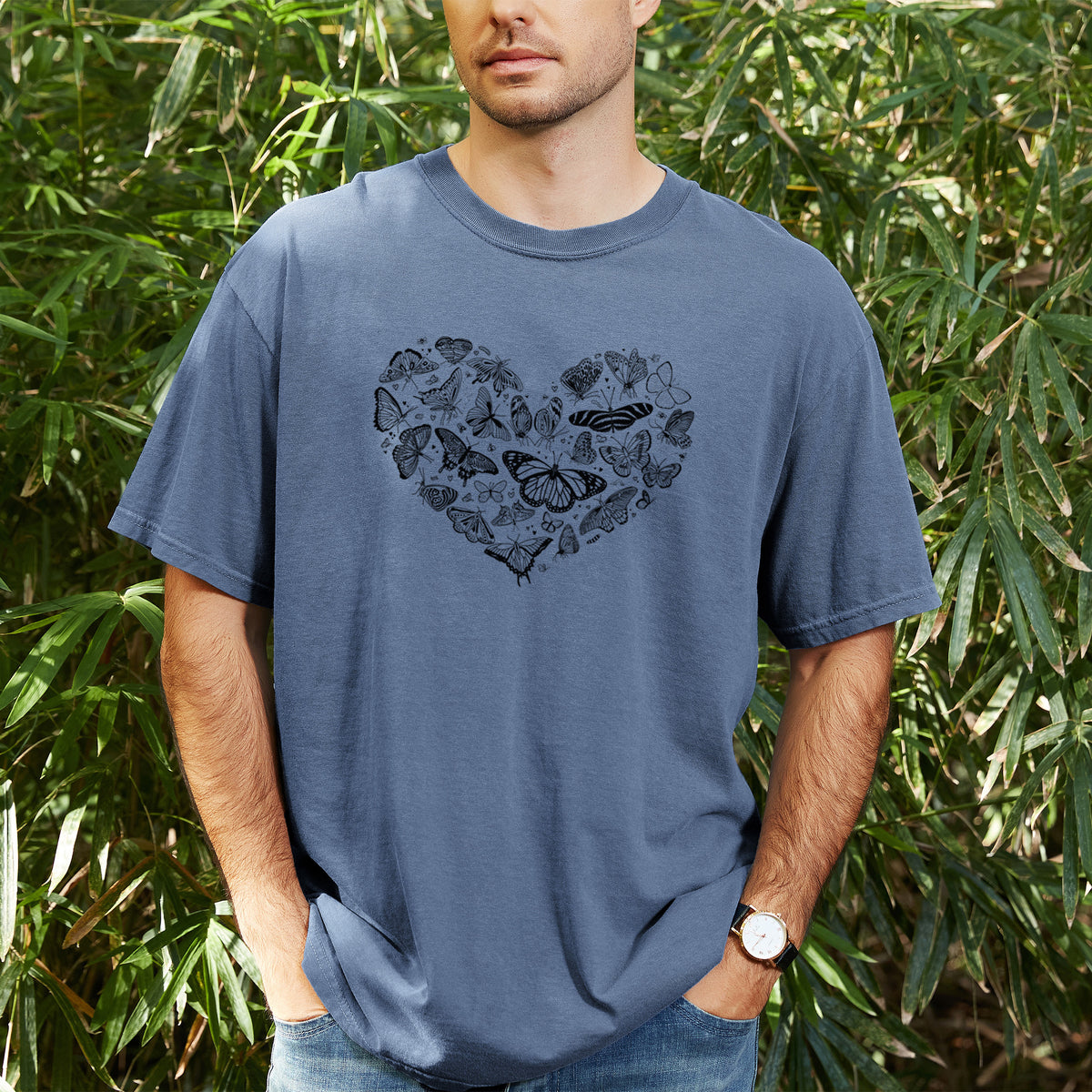 Man wearing a Comfort Colors t-shirt printed with a heart shape filled with small black ink butterflies and moths, outdoors.