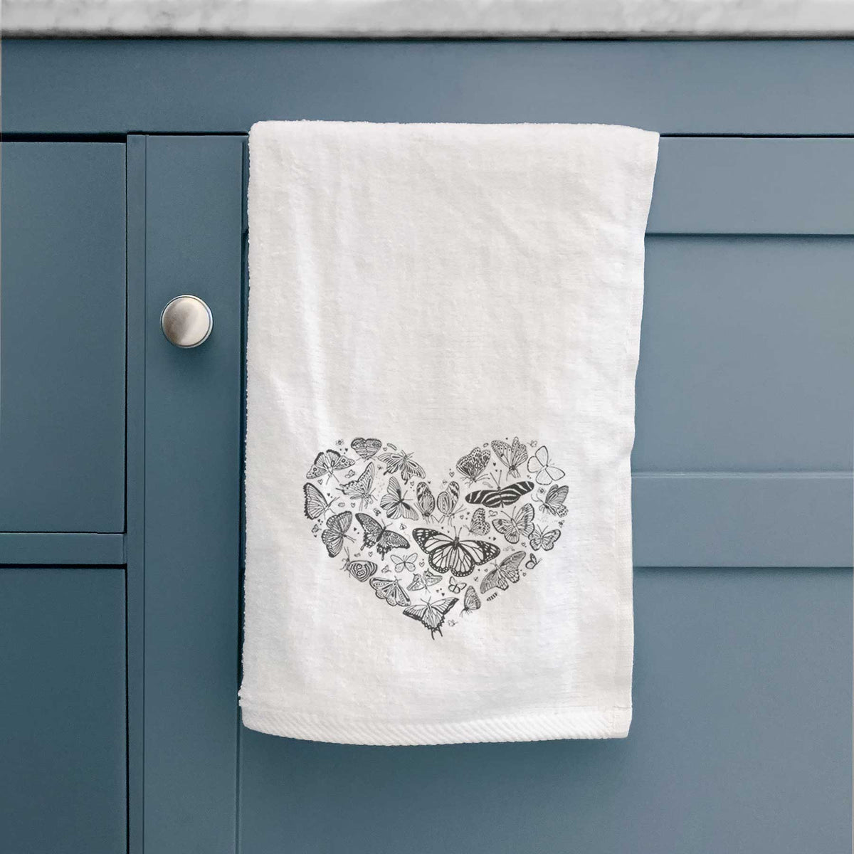 White hand towel printed with a heart shape filled with small black ink butterflies and moths, hanging on a cabinet door.