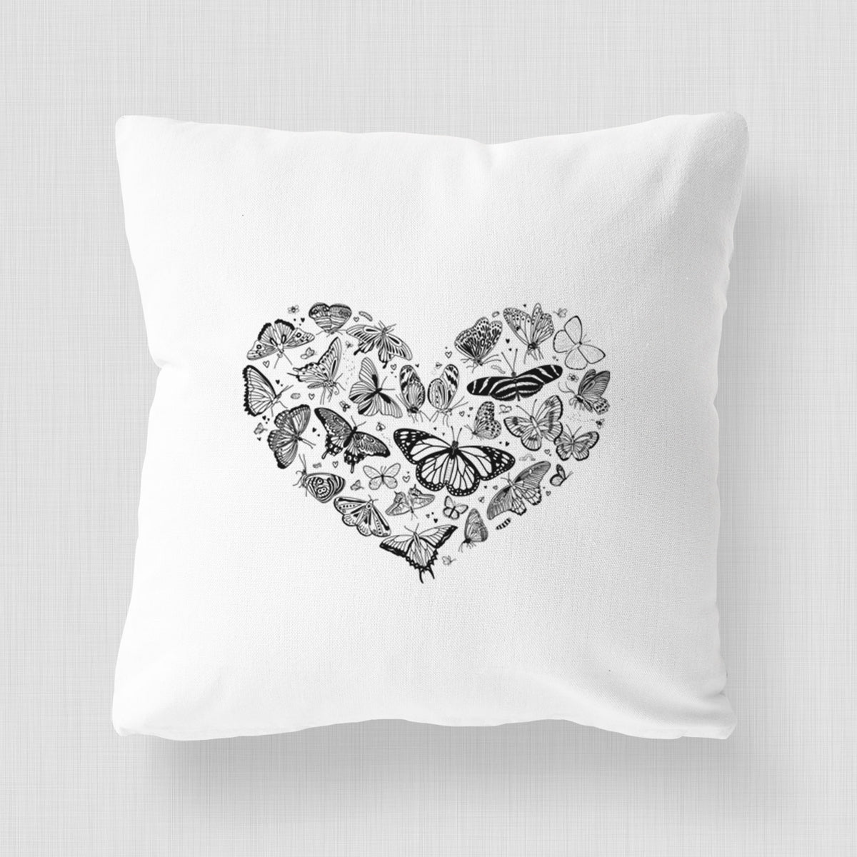 White pillow cover printed with a heart shape filled with small black ink butterflies and moths.