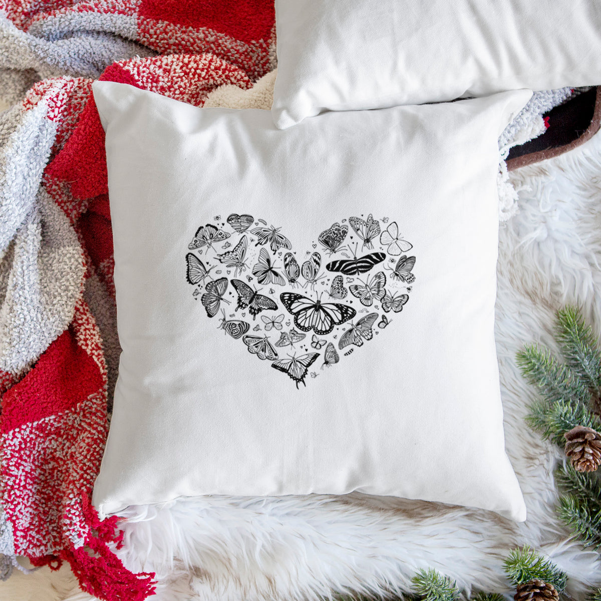 White pillow cover printed with a heart shape filled with small black ink butterflies and moths, on a woven chair.