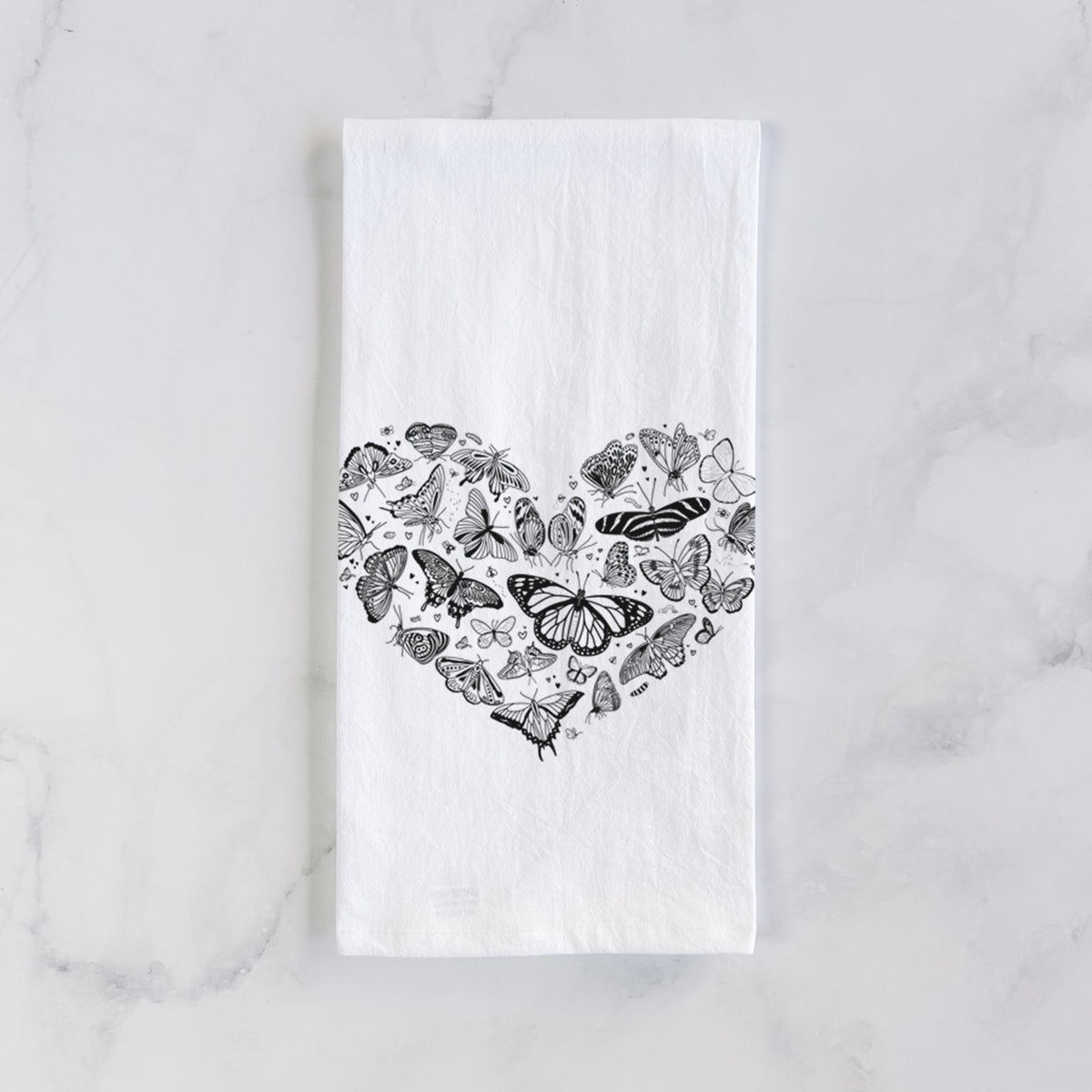 White cotton tea towel laid flat on marble, printed with a heart shape filled with small black ink butterflies and moths.