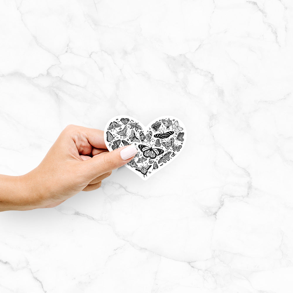 Hand holding a 4 inch vinyl decal of a heart shape filled with small black ink butterflies and moths.