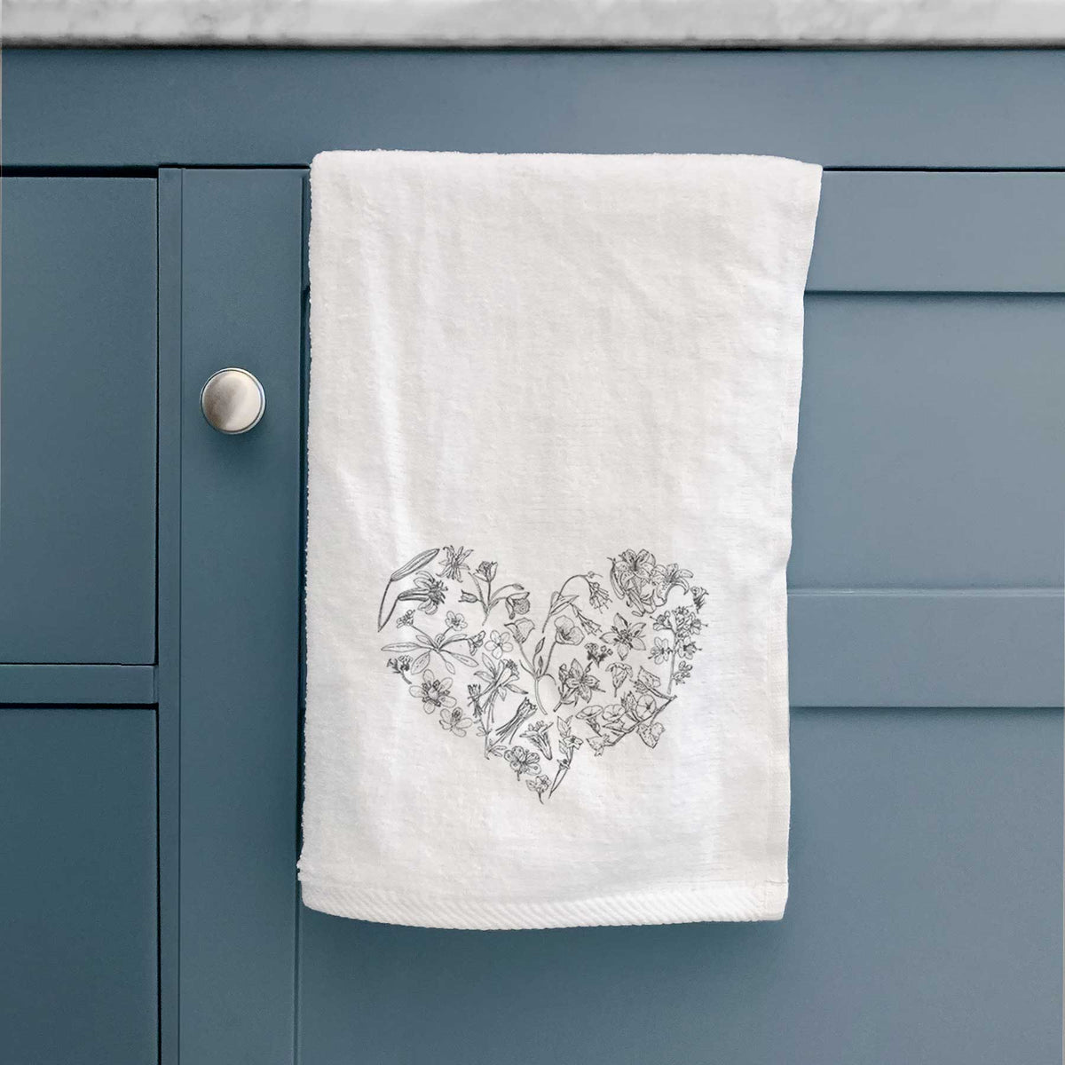 White hand towel printed with a heart shape filled with black ink California mountain wildflowers, hanging on a cabinet door.