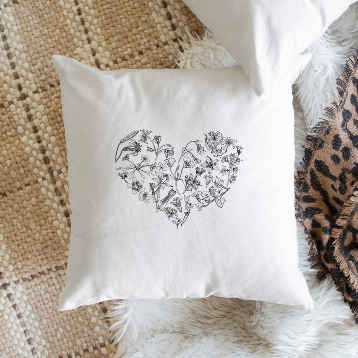 White pillow cover printed with a heart shape filled with black ink California mountain wildflowers, on a woven chair.