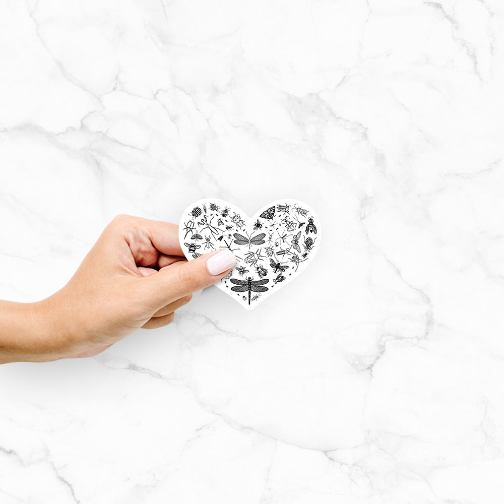 Hand holding a 4 inch vinyl decal of a heart shape filled with small black ink insects, including dragonflies, beetles and bees.