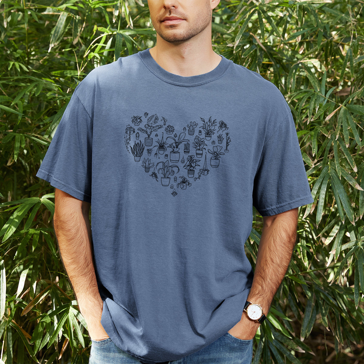 Man wearing a Comfort Colors t-shirt printed with a heart shape filled with black ink potted houseplants, outdoors.