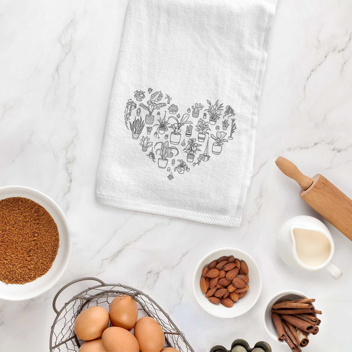 White hand towel printed with a heart shape filled with black ink potted houseplants, hanging on a cabinet door.