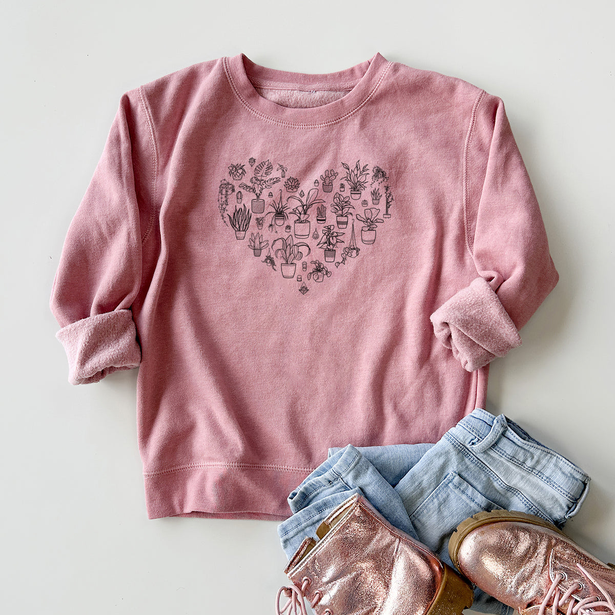 Youth crewneck sweatshirt printed with a heart shape filled with black ink potted houseplants, styled flat with jeans and boots.