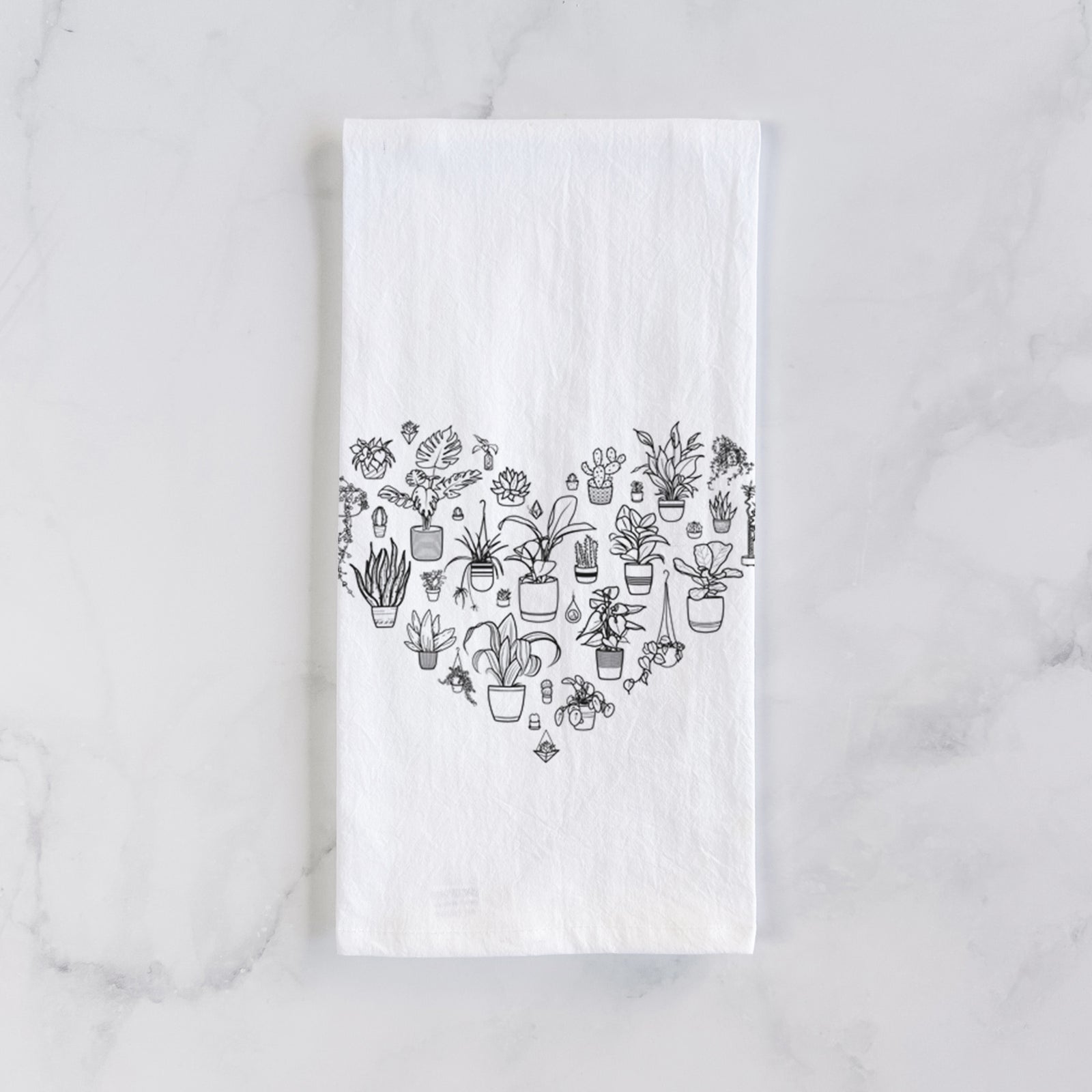 White cotton tea towel printed with a heart shape filled with black ink potted houseplants, on a marble counter beside a round wooden cutting board and greenery.