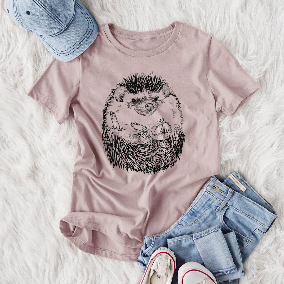 Women's relaxed fit cotton t-shirt printed with a detailed black ink illustration of a hedgehog curled up and facing forward, styled flat on a white faux fur rug with jeans.