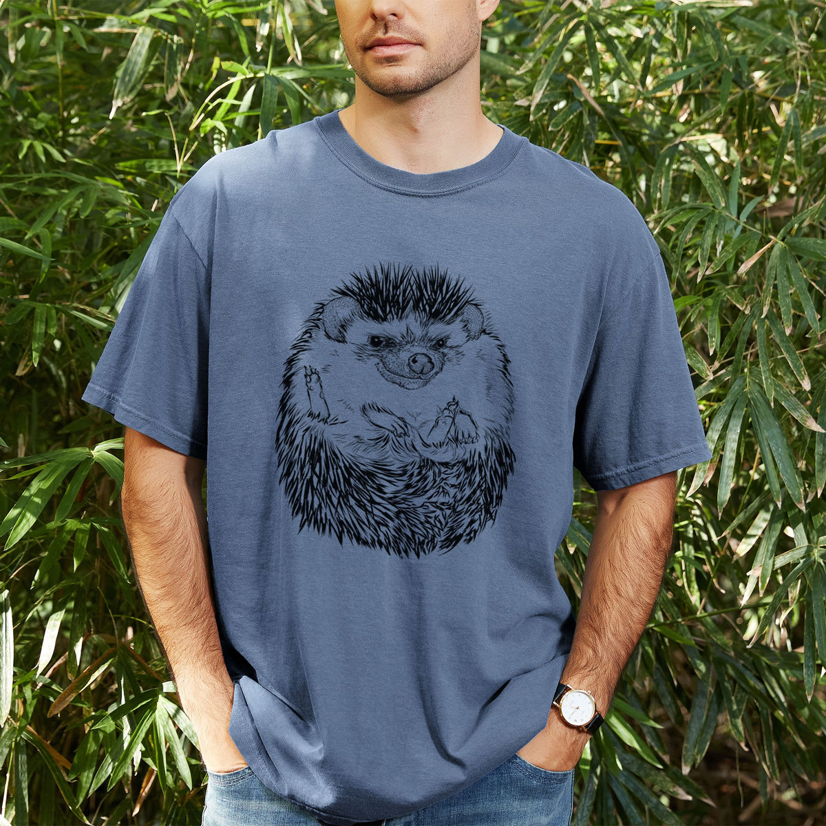 Man wearing a Comfort Colors t-shirt printed with a detailed black ink illustration of a hedgehog curled up and facing forward, outdoors.