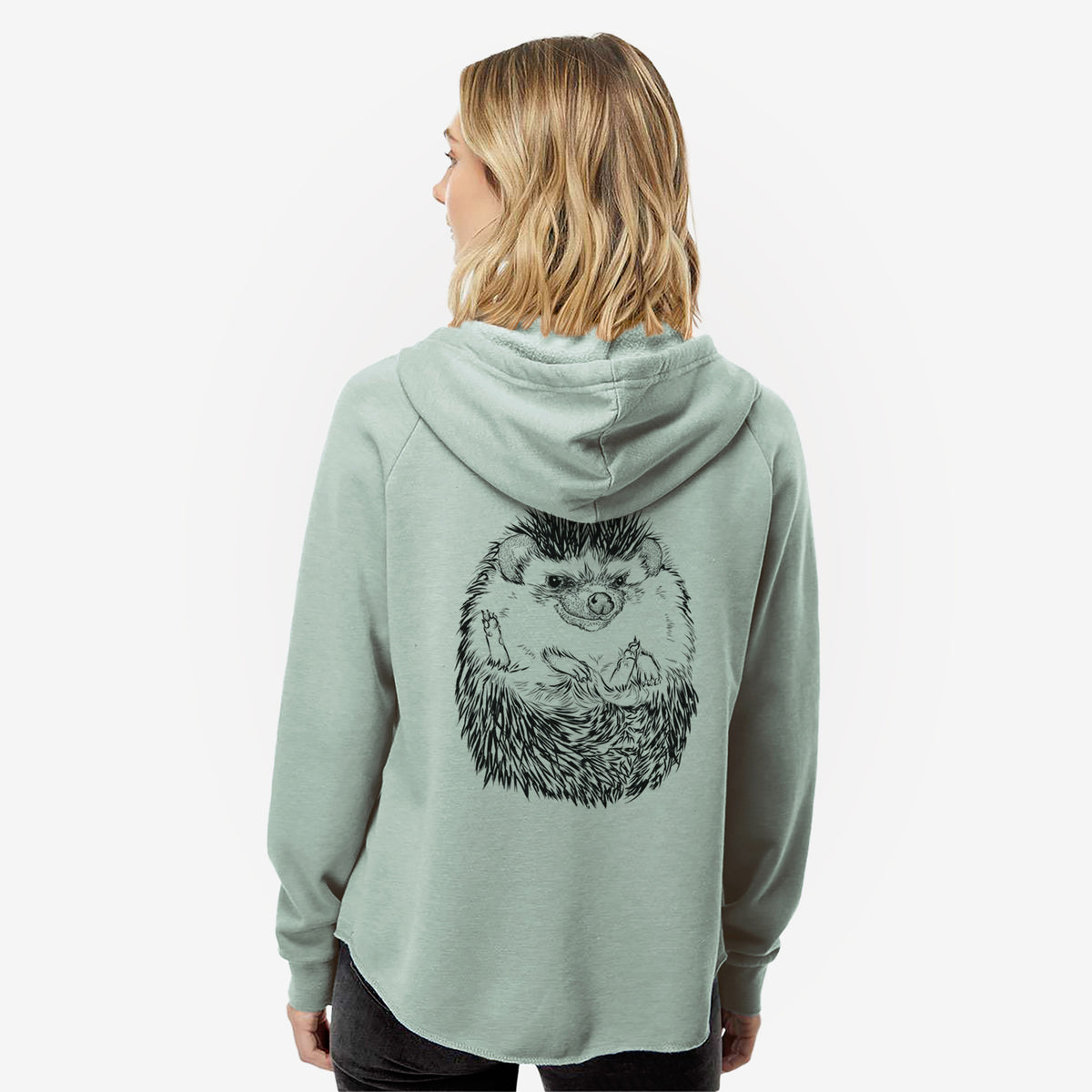 Woman wearing a sage green women's Cali Wave zip-up sweatshirt printed with a detailed black ink illustration of a hedgehog curled up and facing forward, seen from behind.