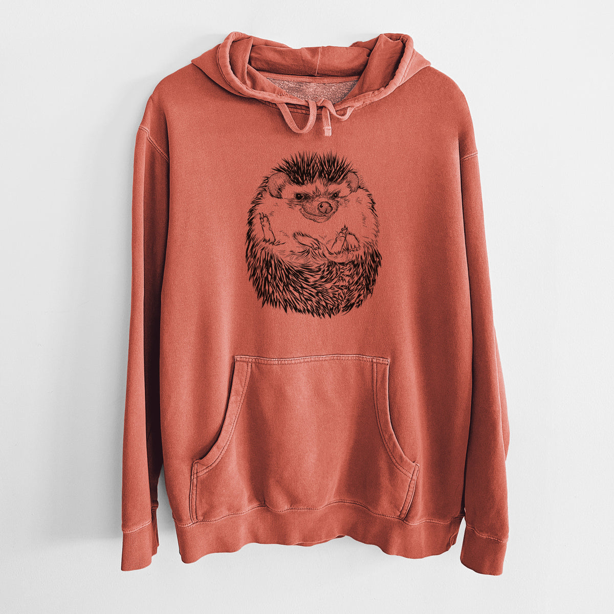 Amber orange pigment dyed hoodie laid flat, printed with a detailed black ink illustration of a hedgehog curled up and facing forward.