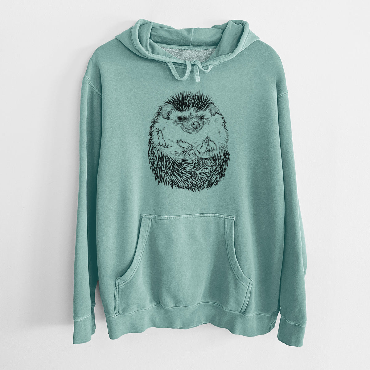 Mint green pigment dyed hoodie laid flat, printed with a detailed black ink illustration of a hedgehog curled up and facing forward.