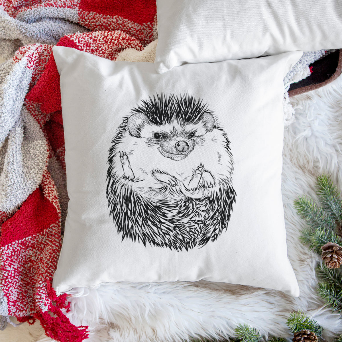 White pillow cover printed with a detailed black ink illustration of a hedgehog curled up and facing forward, on a woven chair.