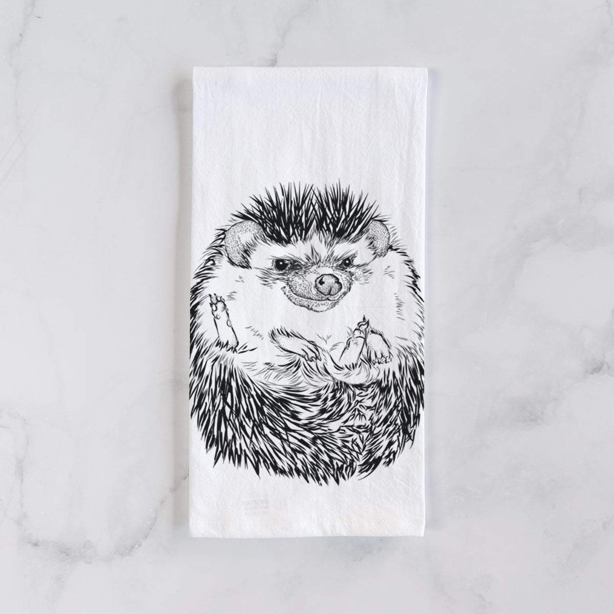 White cotton tea towel laid flat on marble, printed with a detailed black ink illustration of a hedgehog curled up and facing forward.