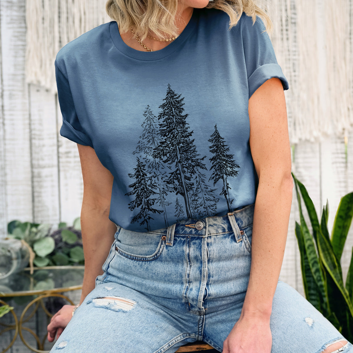 Woman wearing a steel blue lightweight cotton t-shirt printed with a black ink illustration of a forest of tall hemlock trees.