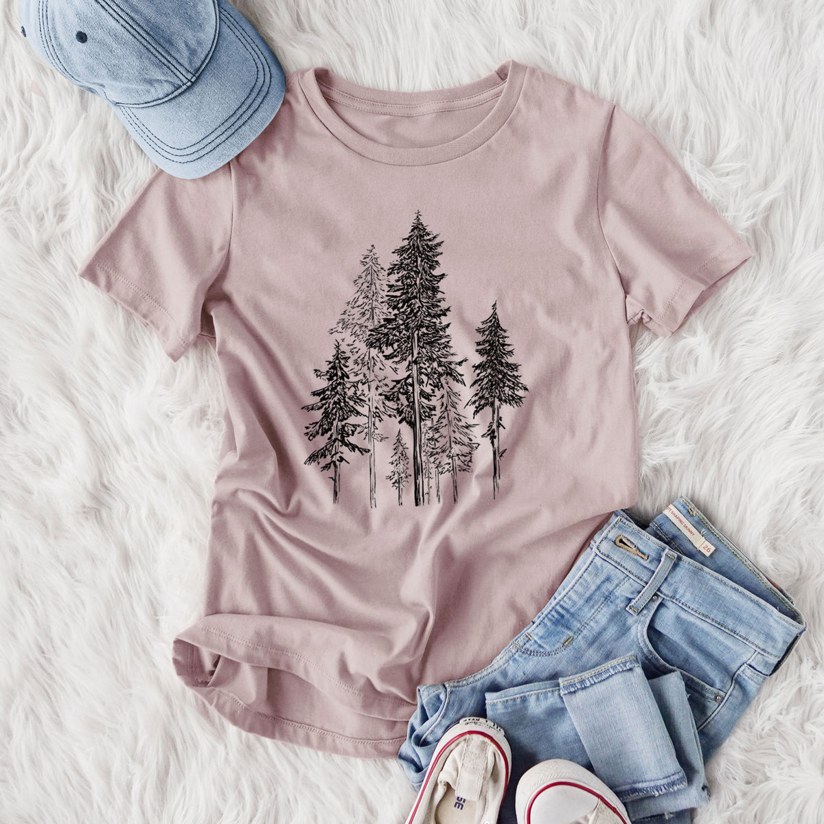 Women's relaxed fit cotton t-shirt printed with a black ink illustration of a forest of tall hemlock trees, styled flat on a white faux fur rug with jeans.